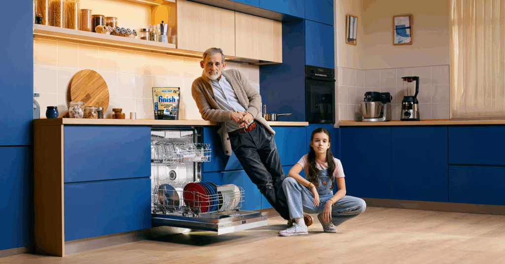 Un abuelo y su nieta en una cocina moderna azul delante de un lavavajillas Bosch abierto, y hay un paquete de Finish en la encimera