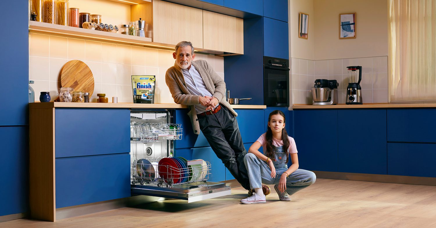 Un abuelo y su nieta en una cocina moderna azul delante de un lavavajillas Bosch abierto, y hay un paquete de Finish en la encimera