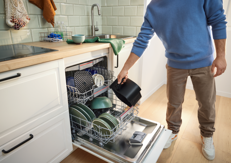 Hombre metiendo las piezas de la Freidora de aire Serie 4 de Bosch en el lavavajillas.